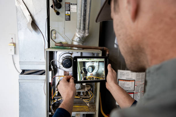 Young Male Property Inspector Photographing a Furnace Hot Water Heater and Air Conditioning Unit Inside a Residential Home Garage stock photo