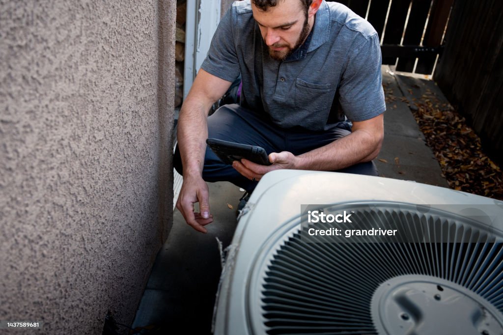 Young Male Property Inspector Photographing a Line to a Residential Air Conditioner Condenser Unit at the side of a stucco home Air Conditioner Stock Photo