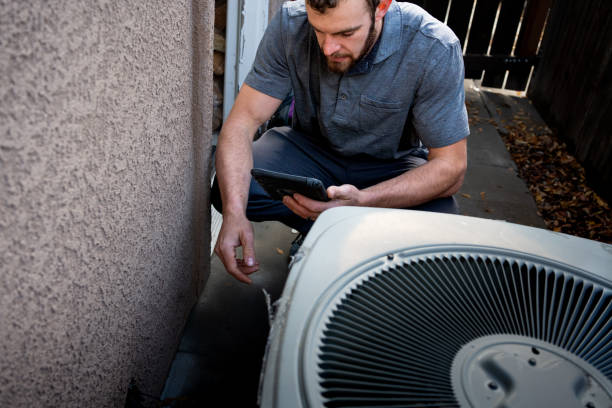 Young Male Property Inspector Photographing a Line to a Residential Air Conditioner Condenser Unit at the side of a stucco home stock photo