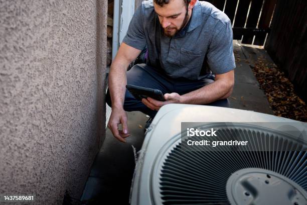 Young Male Property Inspector Photographing A Line To A Residential Air Conditioner Condenser Unit At The Side Of A Stucco Home Stock Photo - Download Image Now