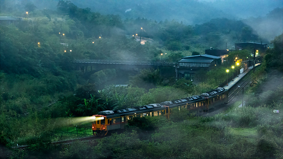 The fog weathertrain traveling in a beautiful valley surrounded by green hills and majestic mountains with a bridge spanning across the river in the fog weather