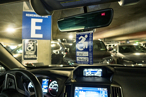 While a cancer patient visits the oncology department inside a hospital, a handicapped parking permit hangs from the inside rear-view mirror of his car parked in a clearly labeled accessible parking spot in the hospital parking garage. NOTE: Other than the handwritten month and year (