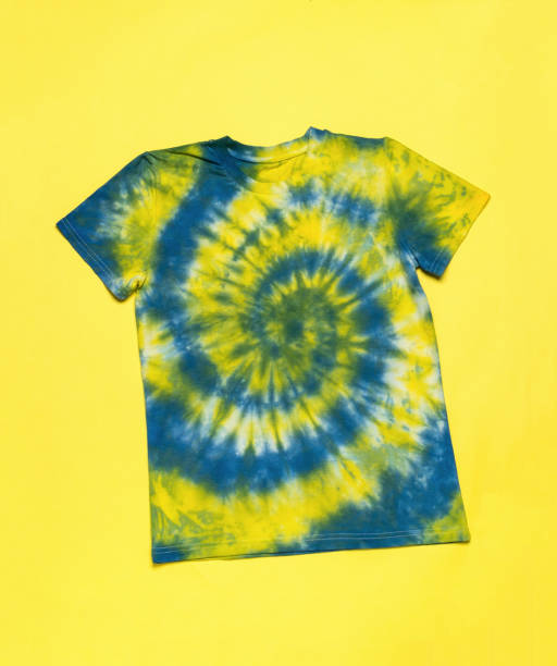 istock Blue and yellow T-shirt with tie dye pattern on a yellow background. Flat lay. 1437605116