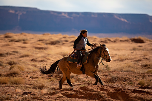 Navajo boy galloping on horse in the Arizona desert - USA
