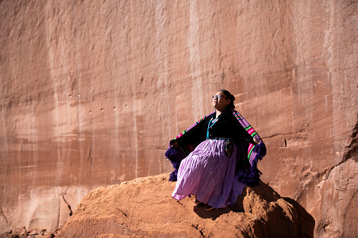 Navajo woman sitting on a rock in with open arms in Monument Valley tribal park