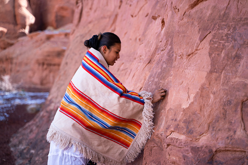 Native american young girl carving into a rock wall in Arizona Monument Valley