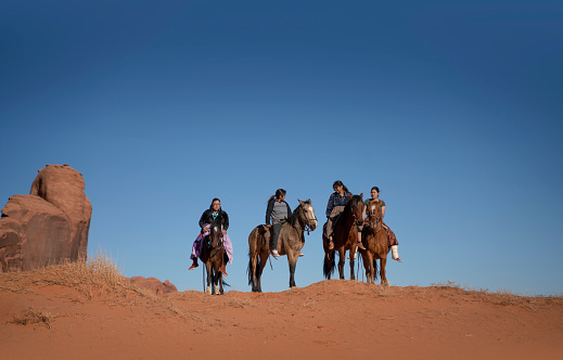 Navajo siblings riding horses on top of a sand hill Monument Valley Arizona