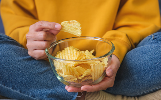 Closeup image of a woman picking and eating potato chips at home