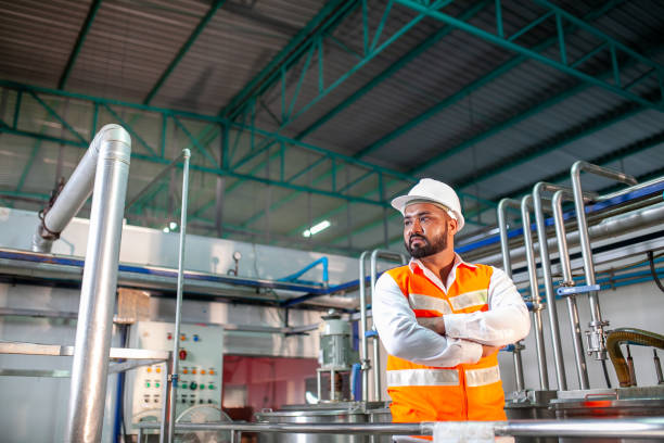 istock Professional engineer with helmet works to maintain industrial construction equipment. Worker is standing in the factory with their arms crossed. 1437608849