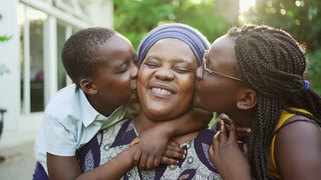 Smiling mom being kissed by her children outside in summer