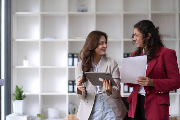 istock Two beautiful Asian businesswomen standing using digital tablet consulting and analyzing information in office work. 1437627419
