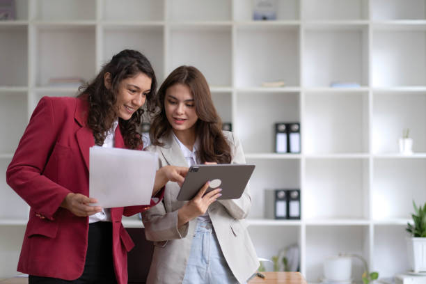 istock Two beautiful Asian businesswomen standing using digital tablet consulting and analyzing information in office work. 1437627427