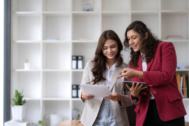 istock Two beautiful Asian businesswomen standing using digital tablet consulting and analyzing information in office work. 1437627444