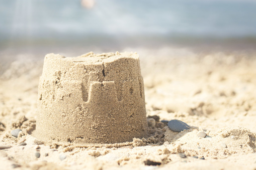 A closeup of a small sandcastle at the beach under the sunlight with a blurry background
