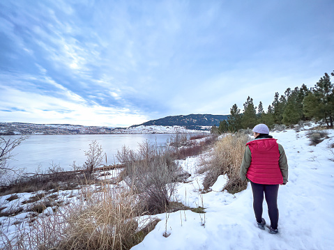 Winter hiking - Eurasian young woman hiking along the waterfront of frozen Lake Nicola, Merritt, British Columbia, Canada.