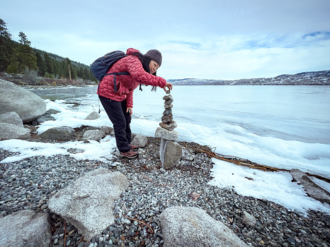 Winter hiking - Chinese woman dismantling a rock cairn found on the waterfront of frozen Lake Nicola, Merritt, British Columbia, Canada.  Leave no trace practice.