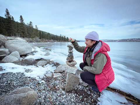 Winter hiking - Eurasian young woman dismantling a rock cairn found on the waterfront of frozen Lake Nicola, Merritt, British Columbia, Canada. Leave no trace practice.