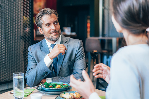 Businessman and businesswoman eating at the restaurant. Business colleagues having lunch together enjoying each other company. Business discussion at the lunch break.