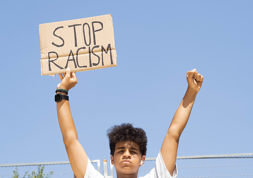 An afro teenage boy with a sign in his hands with the slogan: stop racism