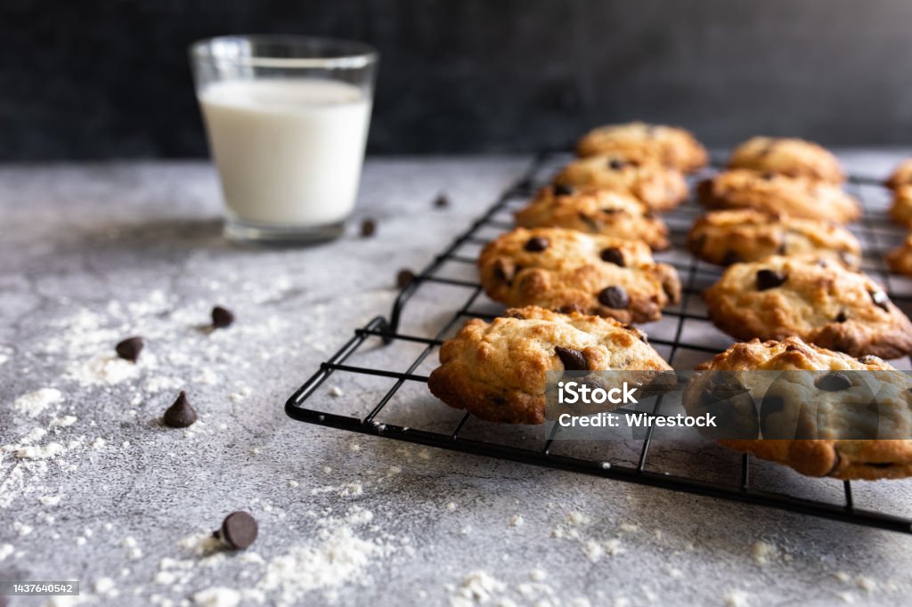 Chocolate Chip Cookies on a cooling rack with a glass of milk Dozen of chocolate chip cookies laying on the cooling rack on a concrete table with dusted flour and glass of whole milk Chocolate Chip Cookie Stock Photo