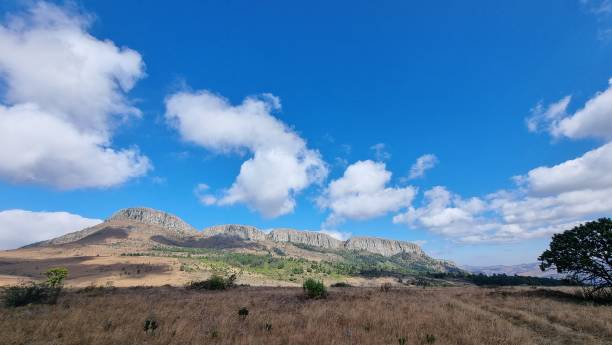 istock Blue cloudy sky over a rock mountain with a dry grass field in the front 1437642636