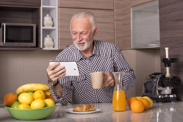 istock Retired elderly male watching a video on a tablet and drinking a cup of coffee in a kitchen 1437644076