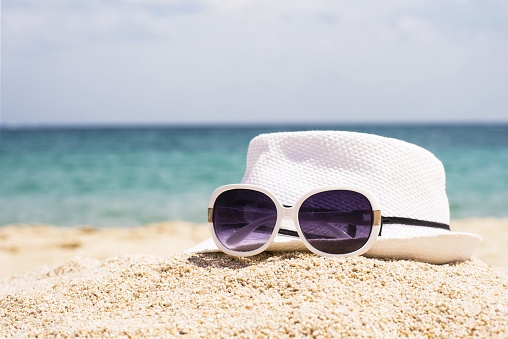 A selective focus shot of sunglasses and a white hat on a sandy beach