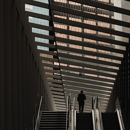 A dramatic scene of a man in a suit at the top of an escalator entering a modern business building