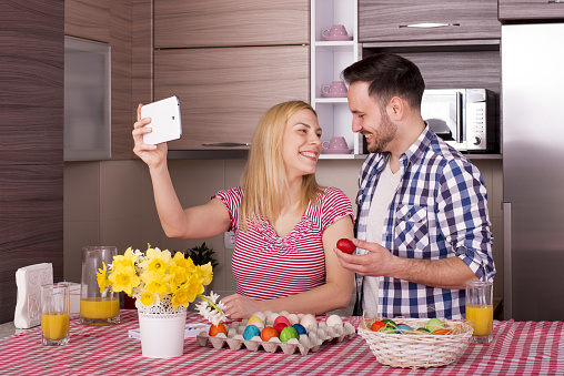 A shallow focus shot of a happy couple taking a selfie while painting Easter eggs in joy