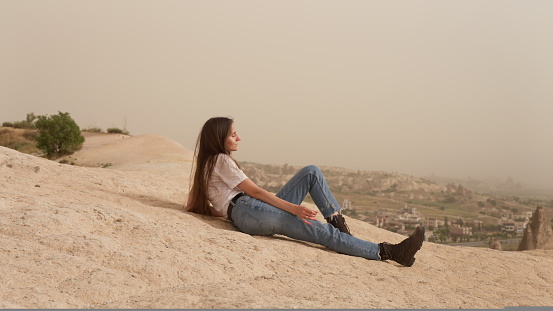 young attractive woman tourist resting on top of a mountain in the desert and watching an epic view from above.
