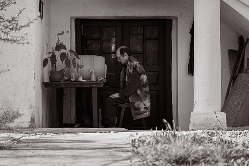 A monochrome photo of one mature retired man having a class of painting with watercolors outdoors of his house.