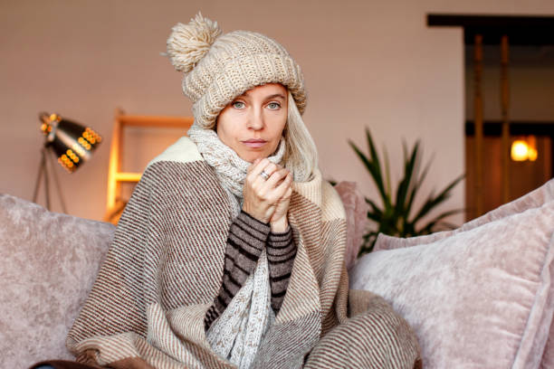 istock Woman warmly clothed and hat in a cold home sitting on couch 1437651782