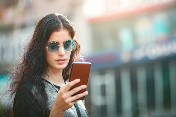 Young woman uses a smartphone standing by the street. stock photo