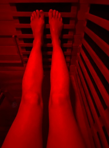 Vertical looking down to legs with feet up in infrared sauna with wood surrounds and red color light therapy