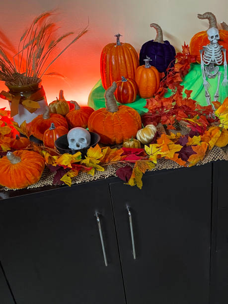 istock Image of Halloween autumn display on cabinet top, artificial plastic and plush gourds surrounded by autumnal coloured fallen leaves, plastic skeleton, cauldron, illuminated string pumpkin lights, focus on foreground 1437654924