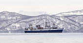The large fishing vessel on the background of snow-covered hills and volcanoes