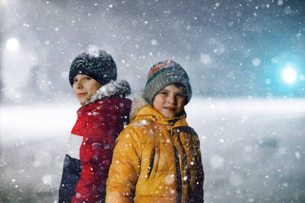 istock Two little kids boys of elementary class walking to school during snowfall on early dark morning. Happy children having fun and playing with first snow. Siblings ans friends in colorful winter clothes 1437657301