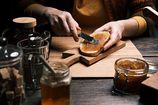 Hands of a woman are preparing a toast with homemade apple marmalade and pouring a glass of hot tea