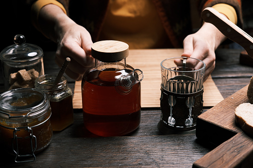 Hands of a woman are preparing a toast with homemade apple marmalade and pouring a glass of hot tea