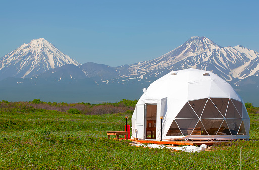 The Glamping house in summer and volcano, rural landscape, tent houses in Kamchatka peninsula. Selective focus.