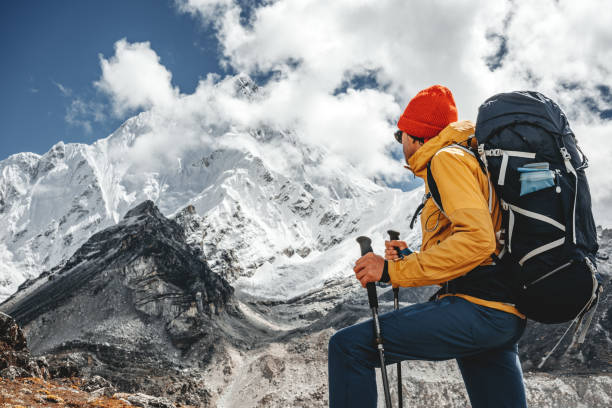 junge touristen wandern auf höhenpfaden zwischen verschneiten und bewölkten bergen. mann expeditor mit reiserucksack geht über steinige wege - himalayas mountain climbing nepal climbing stock-fotos und bilder