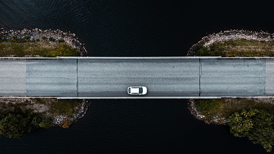 An aerial shot of a white car standing upright in the middle of a bridge