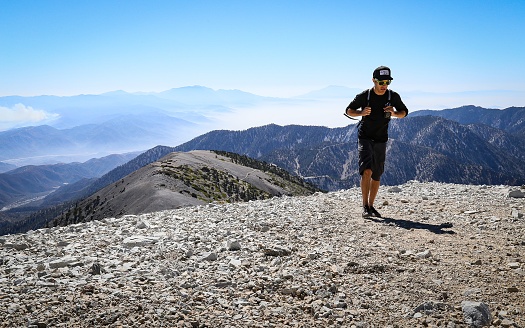 Mt Baldy, California, United States – June 26, 2018: A hiker approaches the top of Mt Baldy with the mountainous landscape cascading behind him.
