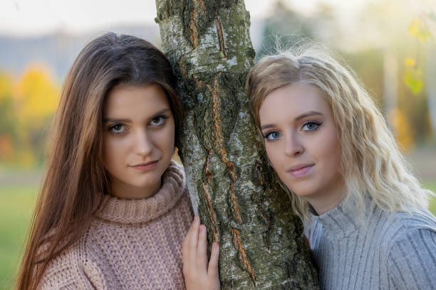Portrait of beautiful two girls posing for the camera in autumn park. Horizontally.