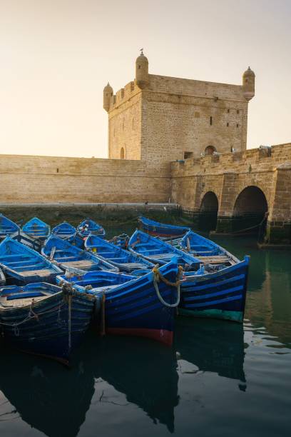 Vertical shot of blue ducked boats in Essaouira harbor Skala Du Port with a pretty skyline A vertical shot of blue ducked boats in Essaouira harbor Skala Du Port with a pretty skyline essaouira stock pictures, royalty-free photos & images