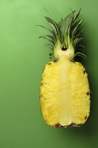 A high angle vertical shot of a cut ripe pineapple isolated o green background with a copy space