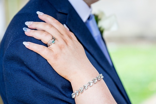 A closeup of a bride's hand with rings on groom's shoulder at a wedding