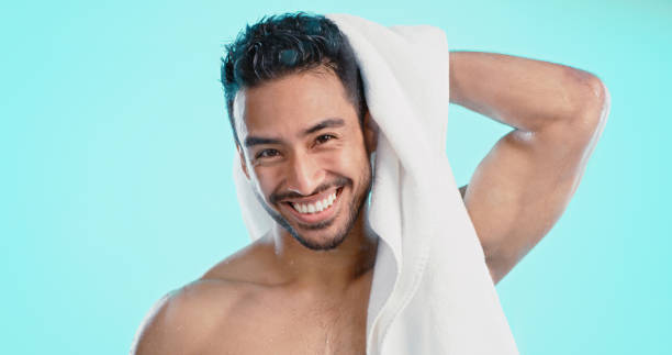 portrait man in shower with towel, healthy skincare and fresh body wellness of clean water on studio blue background. bathroom grooming, cleaning or hygiene of young, strong and happy model guy - sensuality men shirtless studio shot imagens e fotografias de stock