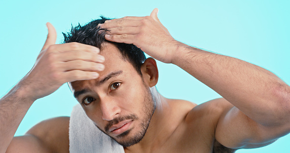 Shower, hair and hygiene with a man cleaning his skin in studio on a blue background for care or wellness. Fresh, haircare and bathroom with a handsome young male washing his face for cleanliness