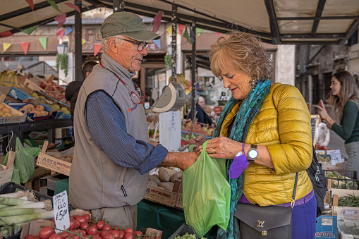 Venice, Italy - October 12th 2022: Middle aged male greengrocer in his market stall with a female customer in the outdoor food market in the center of the old and famous Italian city Venice